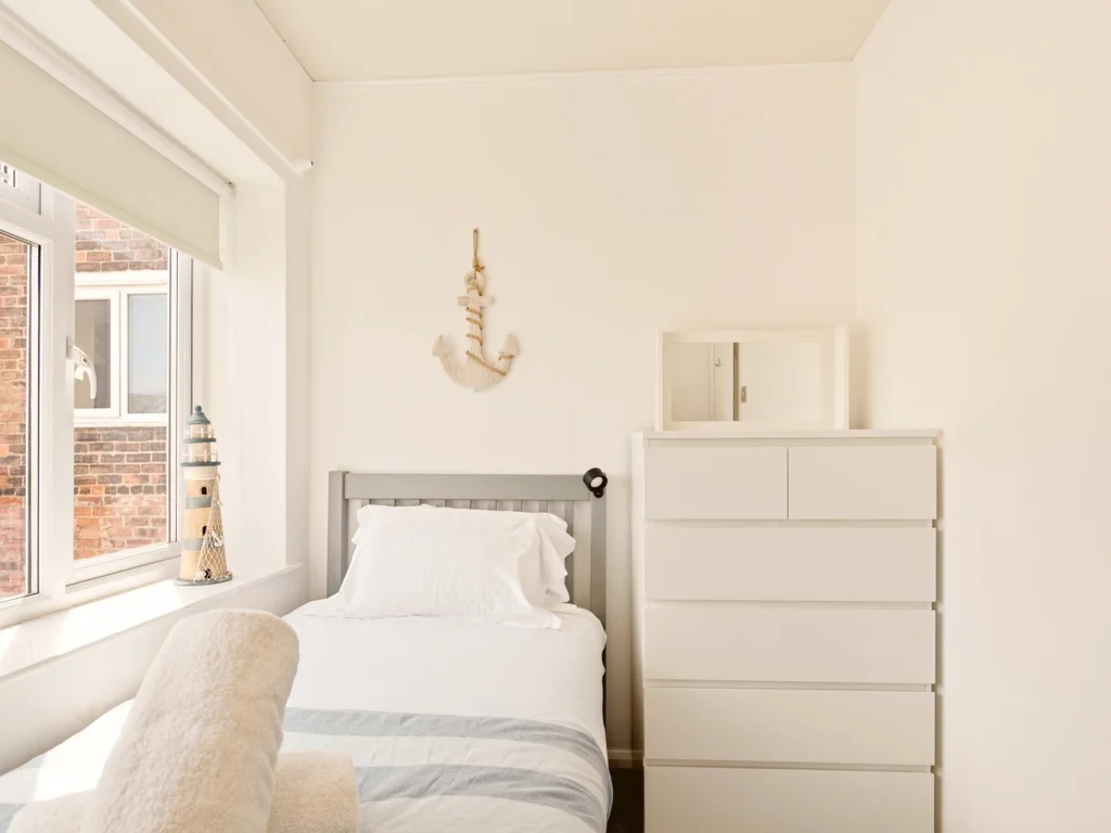 Single bedroom with large window, chest of drawers and nautical accents.