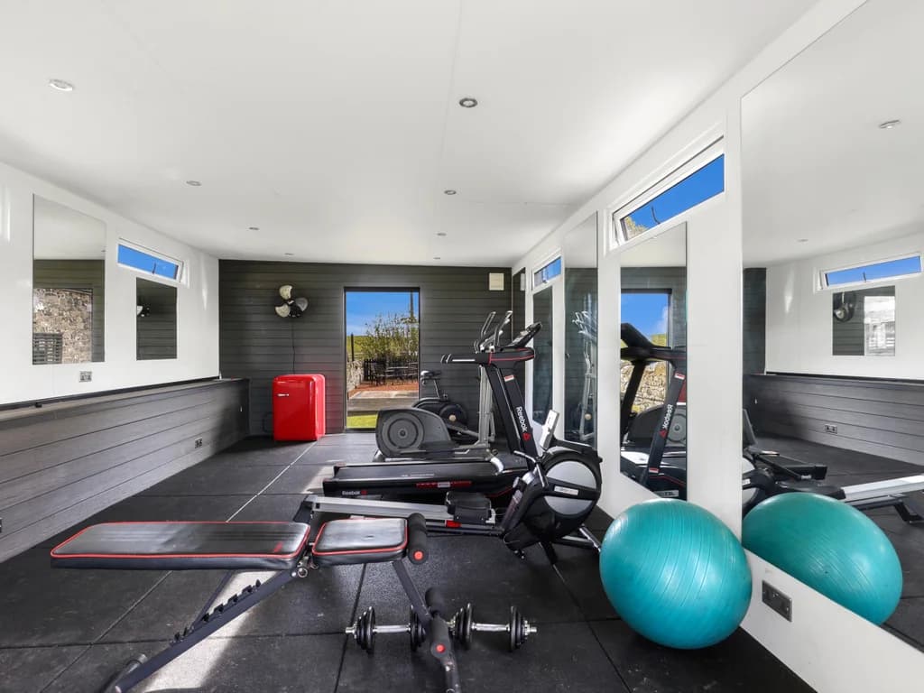 Shared gym with cardio machines, weights bench, mirrors and rubber flooring.